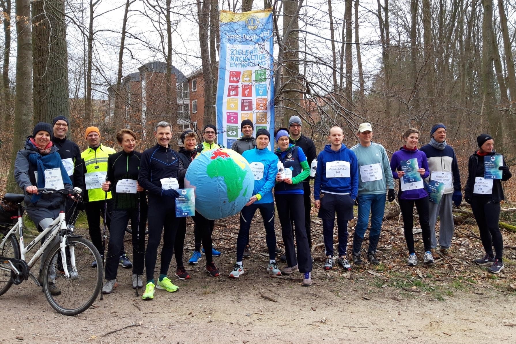 Mitglieder des Lions Club Lüneburg-Ilmenau treffen sich im Wald zum gemeinsamen Lauf. Für das Foto halten Sie einen großen Wasserball in die Höhe, auf dem eine Weltkugel abgebildet ist.