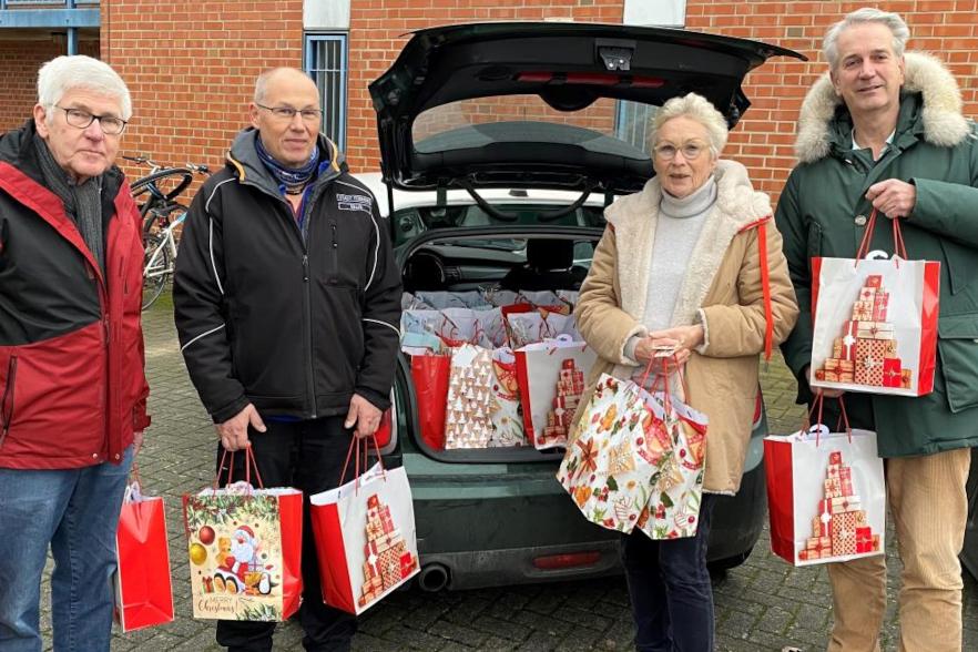 Auf dem Bild sieht man 3 Herren und eine Dame. Sie stehen neben der geöffneten Heckklappe eines PKW. Der zu sehende Kofferraum ist mit den im Artikel benannten Weihnachtstüten befüllt. Die Helfer:innen haben jeweils ein paar Tüten in der Hand, bereit diese an die Wohnungslosen zu übergeben.